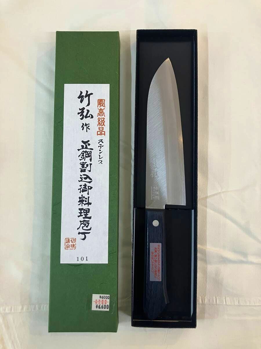A Santoku chef knife in its box alongside a green product box with Japanese labeling, shown against a light background.