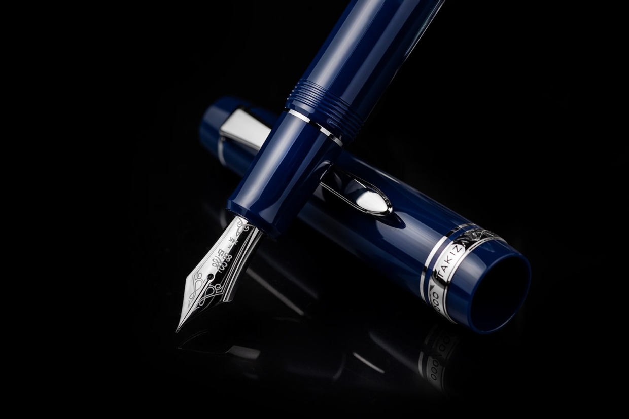 Dark blue fountain pen with its cap beside it, showing the silver nib on a black reflective surface.