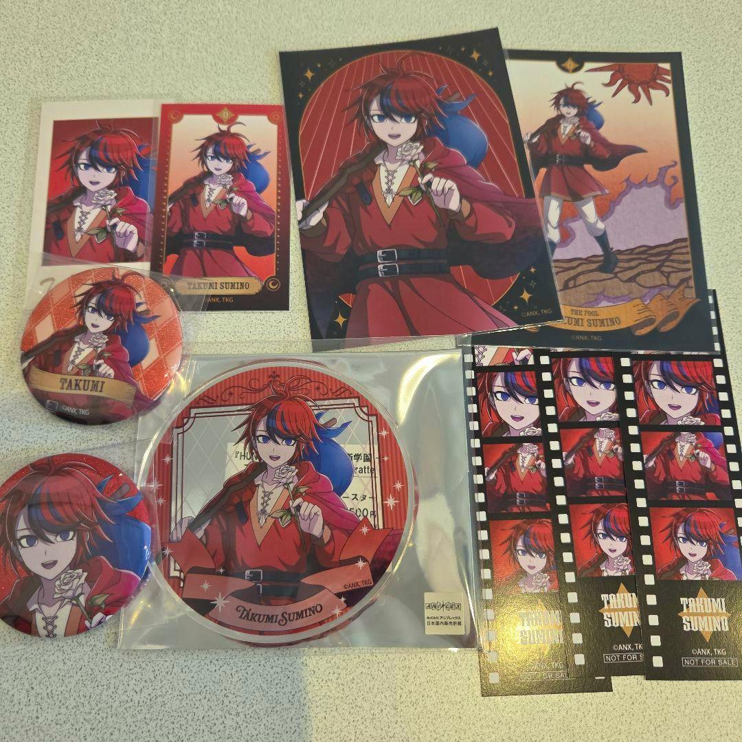 Photo of the acrylic plate and accompanying tarot-set goods showing Takumi Sumino artwork, including a sealed round acrylic plate, badges, cards, and filmstrip-style stickers.