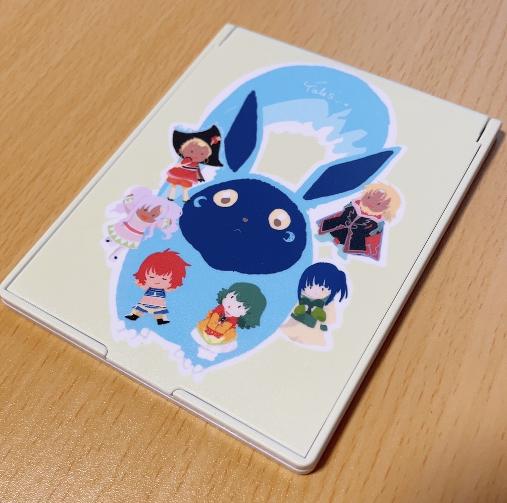 Top view of a folding compact mirror decorated with colorful character stickers on a wooden surface.