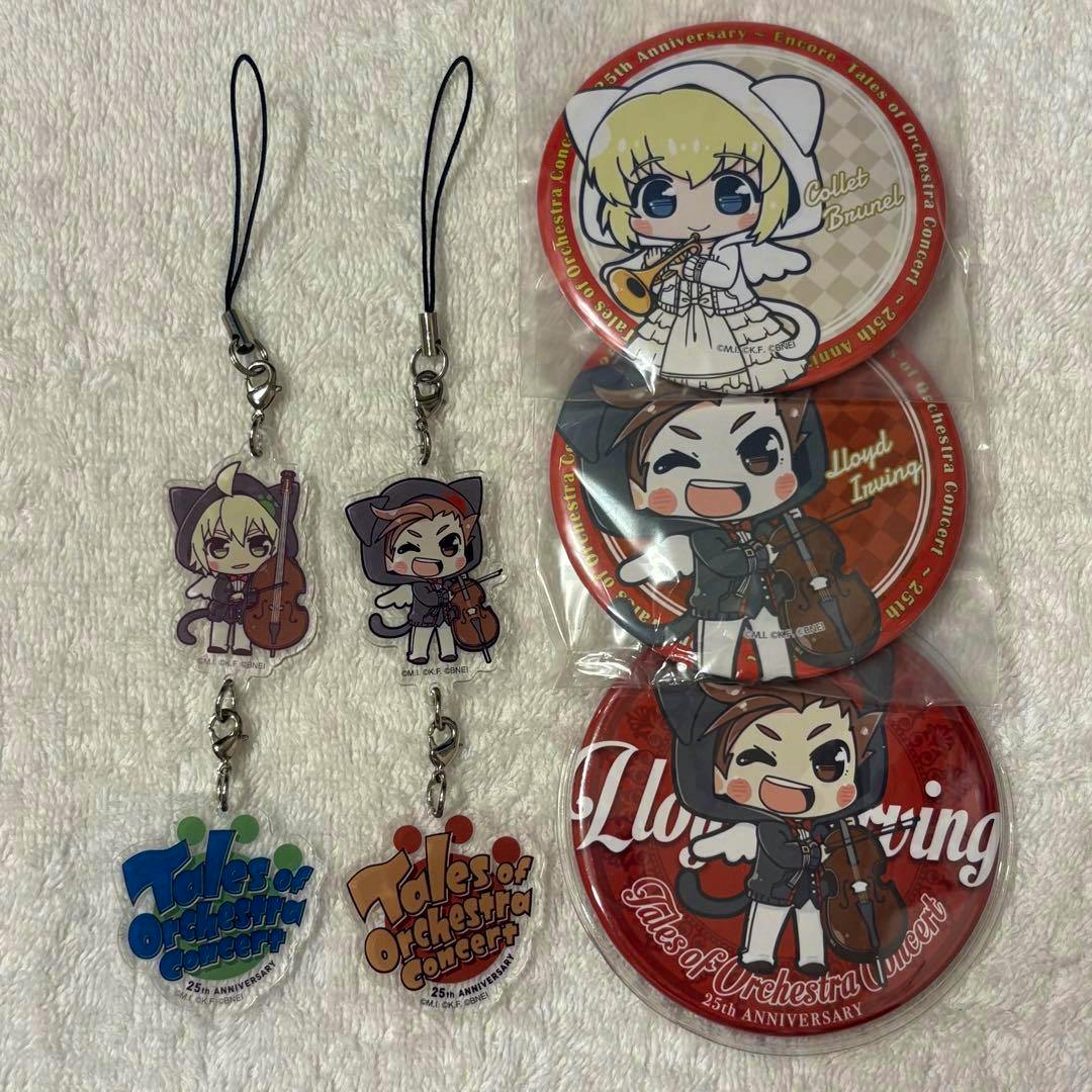 A photo of acrylic keychains and round concert badges featuring chibi characters and "Tales of Orchestra Concert" logos laid on a towel.