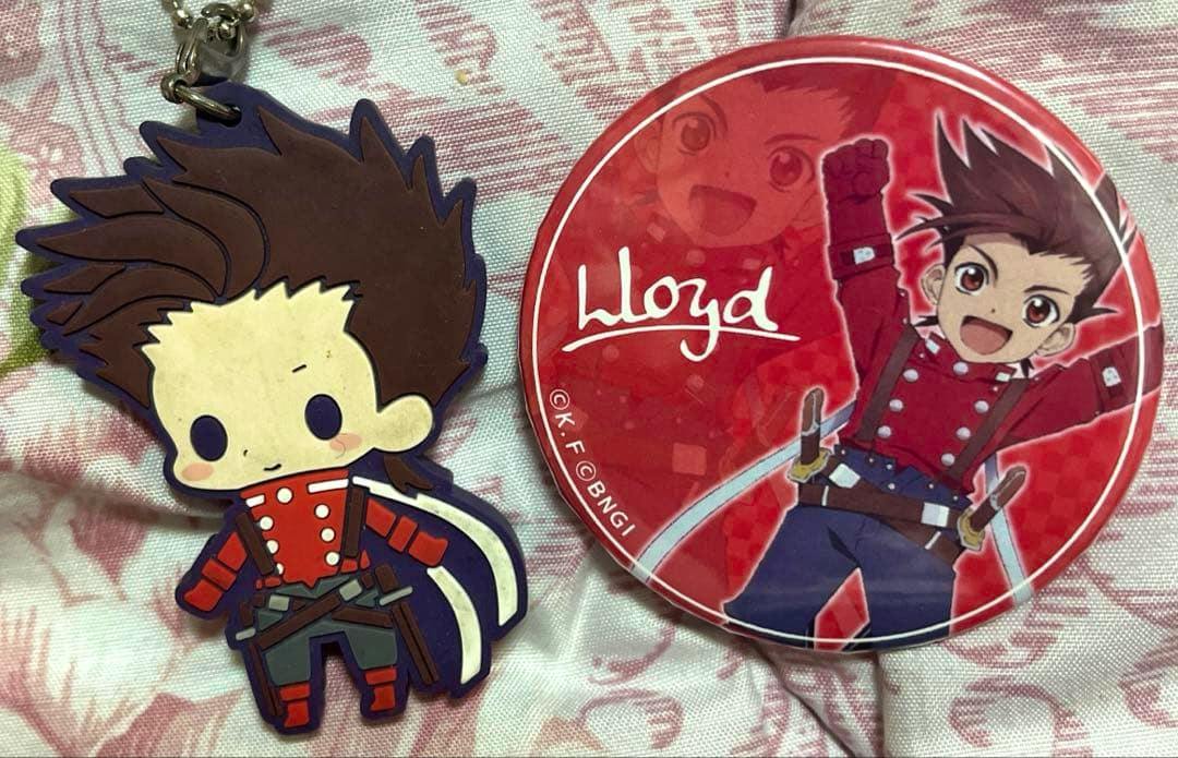 A red round badge featuring Lloyd from Tales of Symphonia alongside a chibi Lloyd rubber keychain charm placed on fabric.