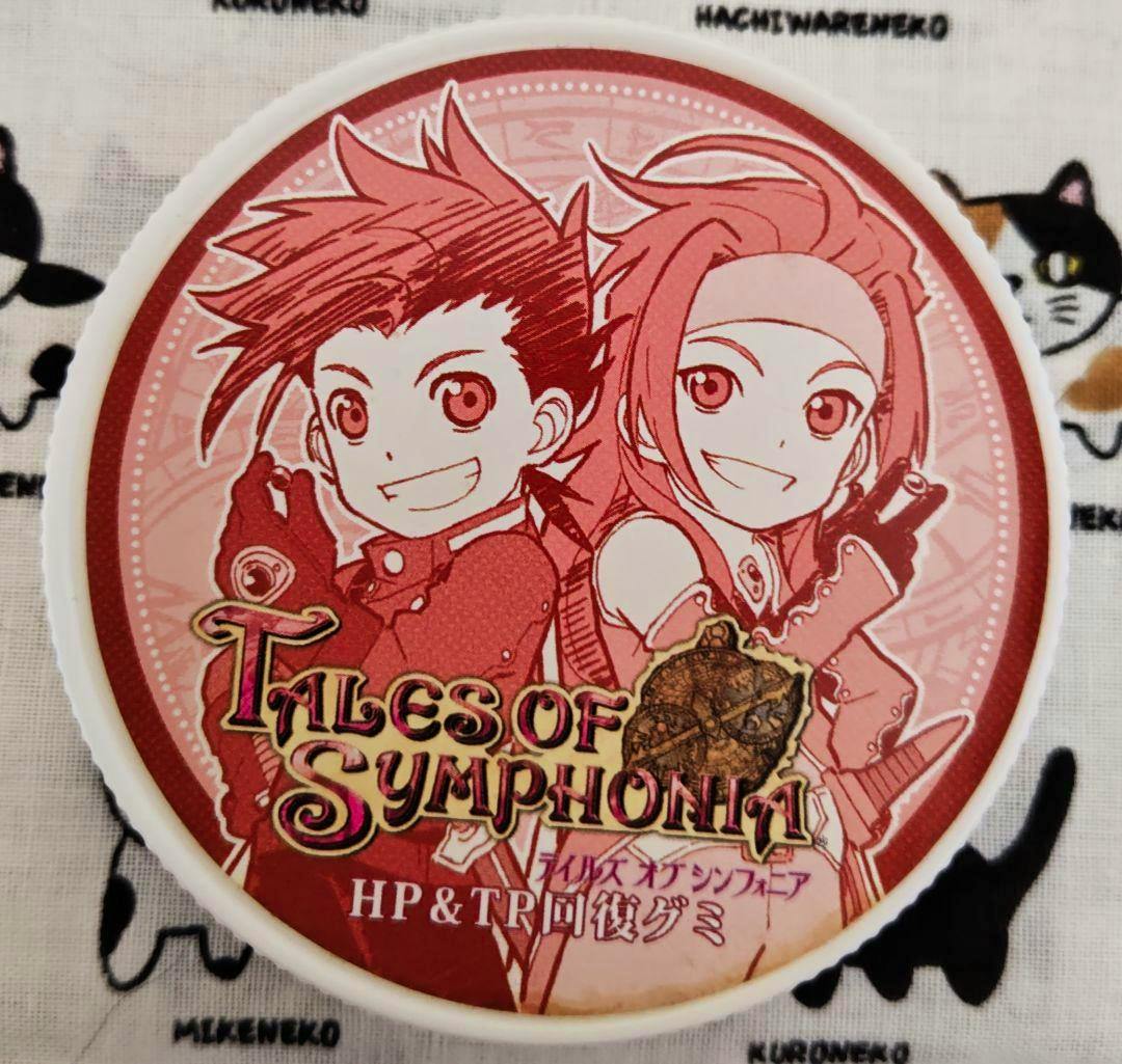 Plastic lid (cover) for the product showing red-toned printed artwork of Lloyd and Zelos with the "Tales of Symphonia" logo.
