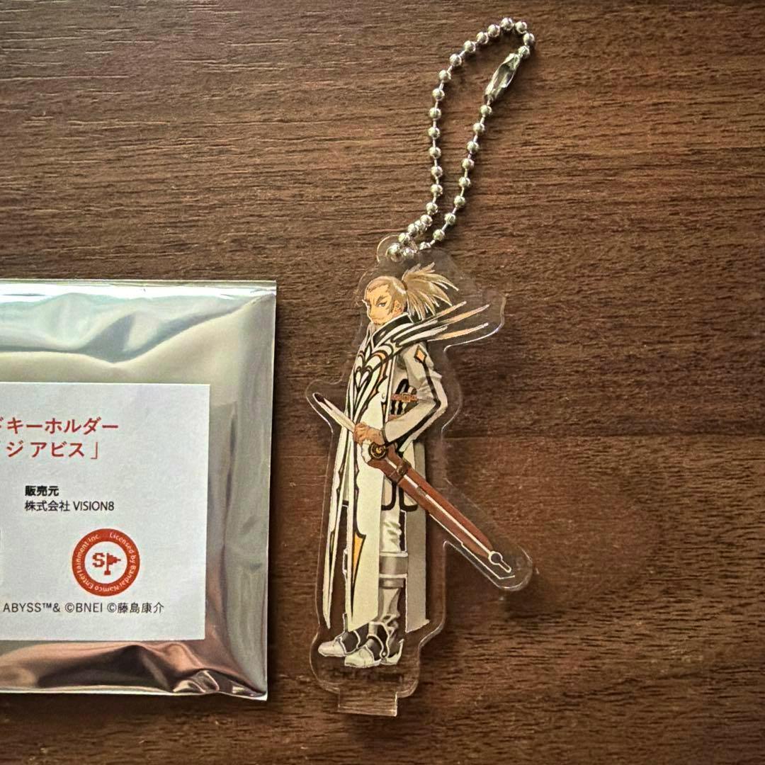 Acrylic stand keychain of Van from Tales of the Abyss with its ball chain beside silver packaging on a wooden surface.