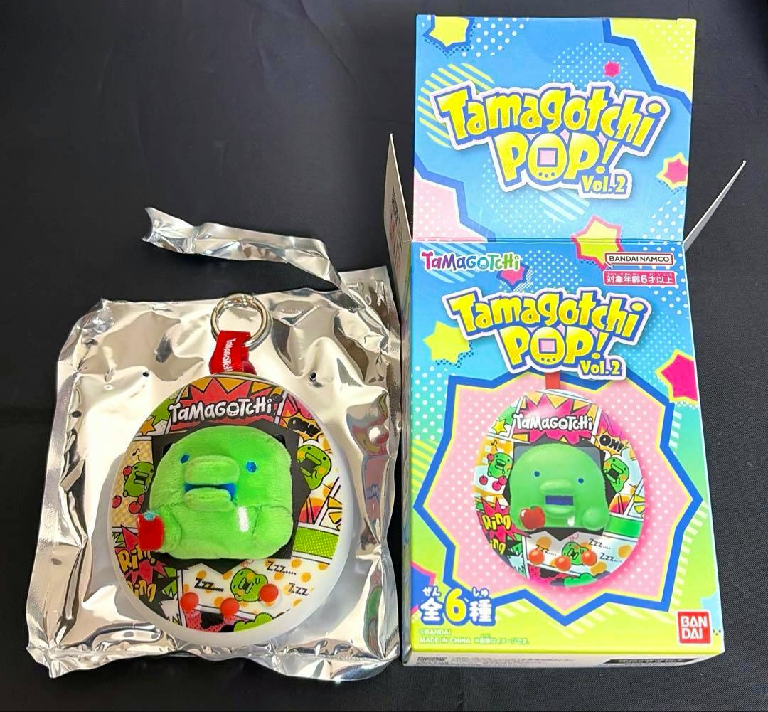 Green Tamagotchi POP Vol.2 plush keychain (くちぱっち) in silver packaging shown beside its colorful Tamagotchi POP! Vol.2 box.
