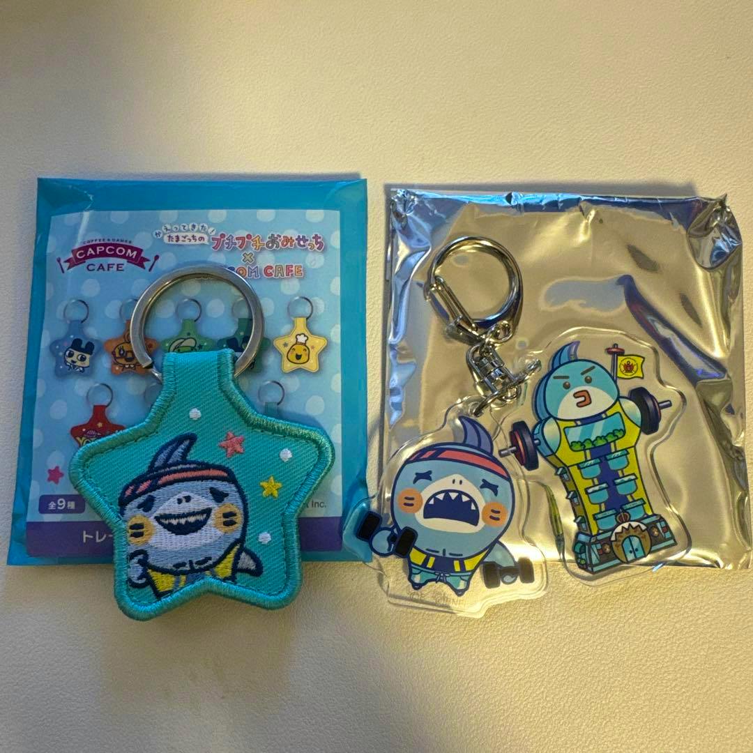 Three Tamagotchi keychains on a light surface: a star-shaped embroidered keychain attached to backing card and two acrylic character keychains, one in metallic packaging.