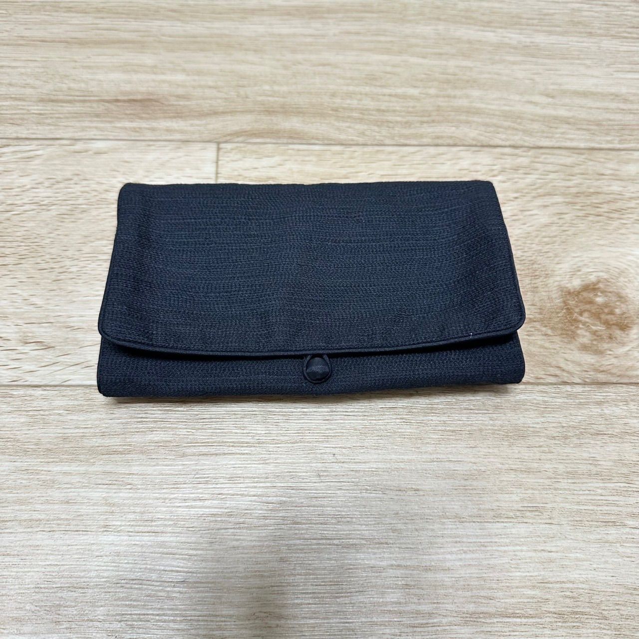 Folded black nylon pouch with a flap and button closure on a wooden surface.