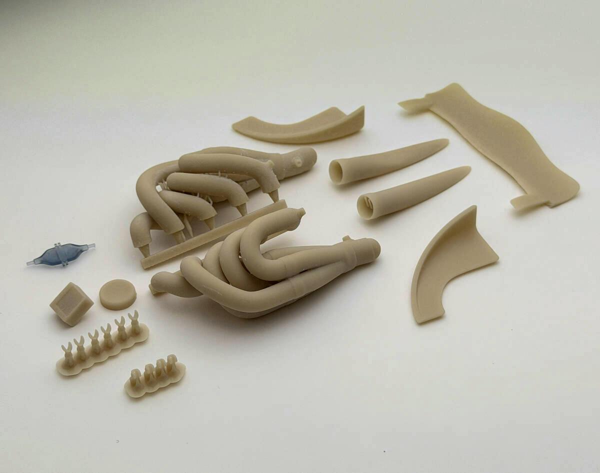 Beige 3D-printed exhaust pipes and small detail-up parts for a TAMIYA 1/12 Williams FW14B model laid out on a white background.