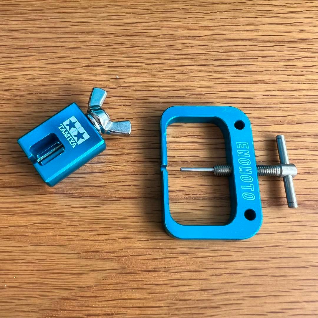 Two blue metal Mini 4WD tools, one marked "TAMIYA" and one marked "ENOMOTO", photographed on a wooden surface.