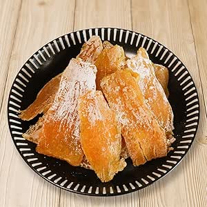 A black plate holding several powdered dried potato slices on a light wooden surface.