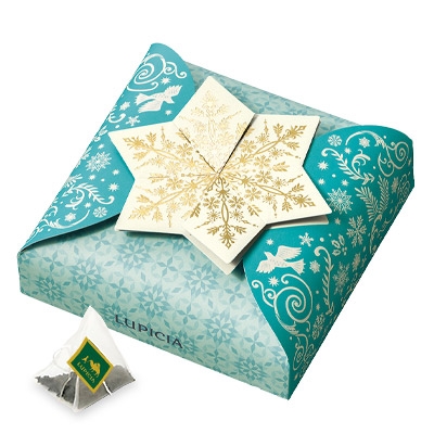 A teal decorative gift box with a gold snowflake star on top and two pyramid black tea bags displayed in front.