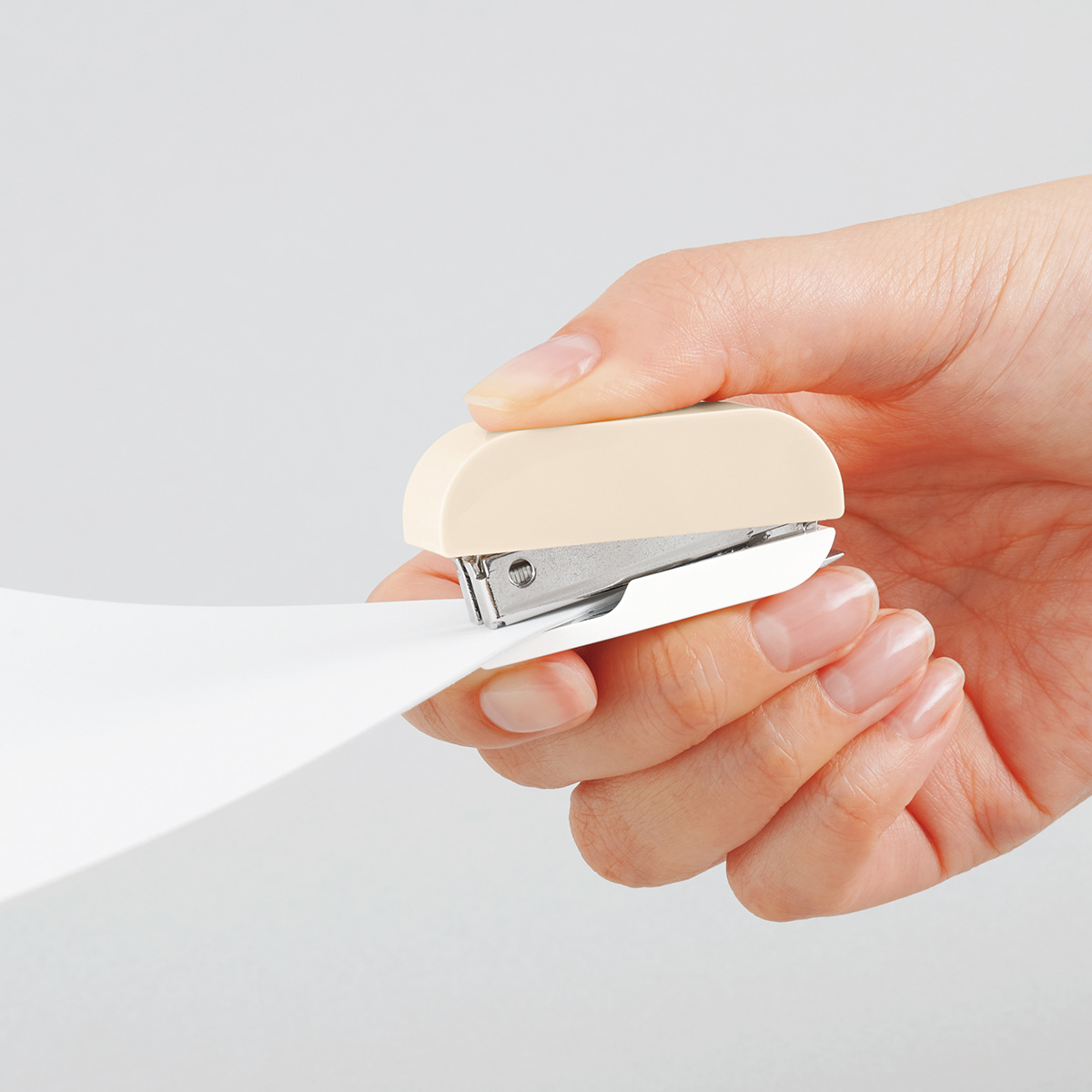 A hand holding a stapler while stapling sheets of paper.