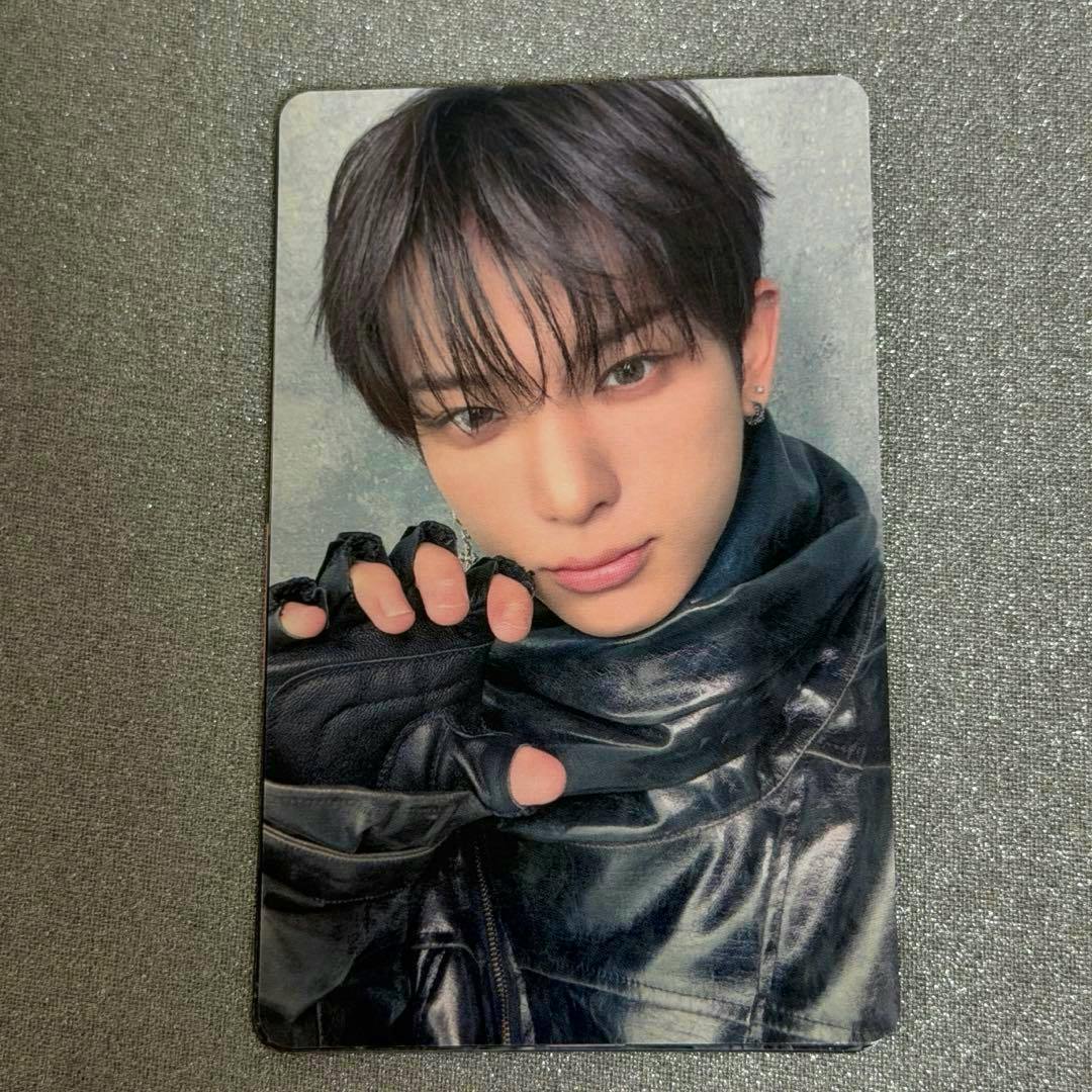 Photocard front showing a close-up portrait of a person wearing a dark shiny jacket and a fingerless glove on a textured gray background.