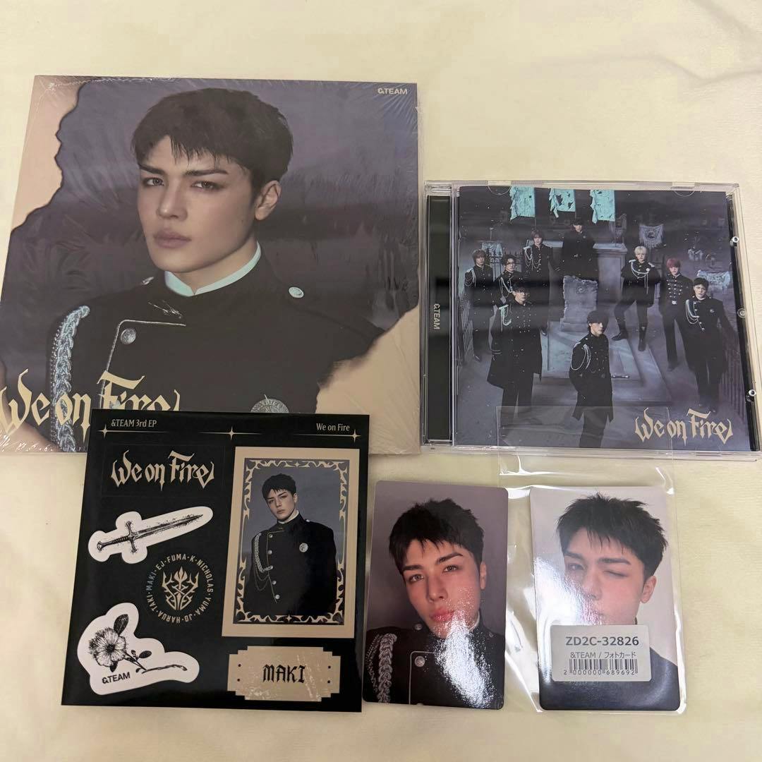 Photo showing the &TEAM CD (We on Fire) jewel case with accompanying MAKI photocards and related merchandise laid out.