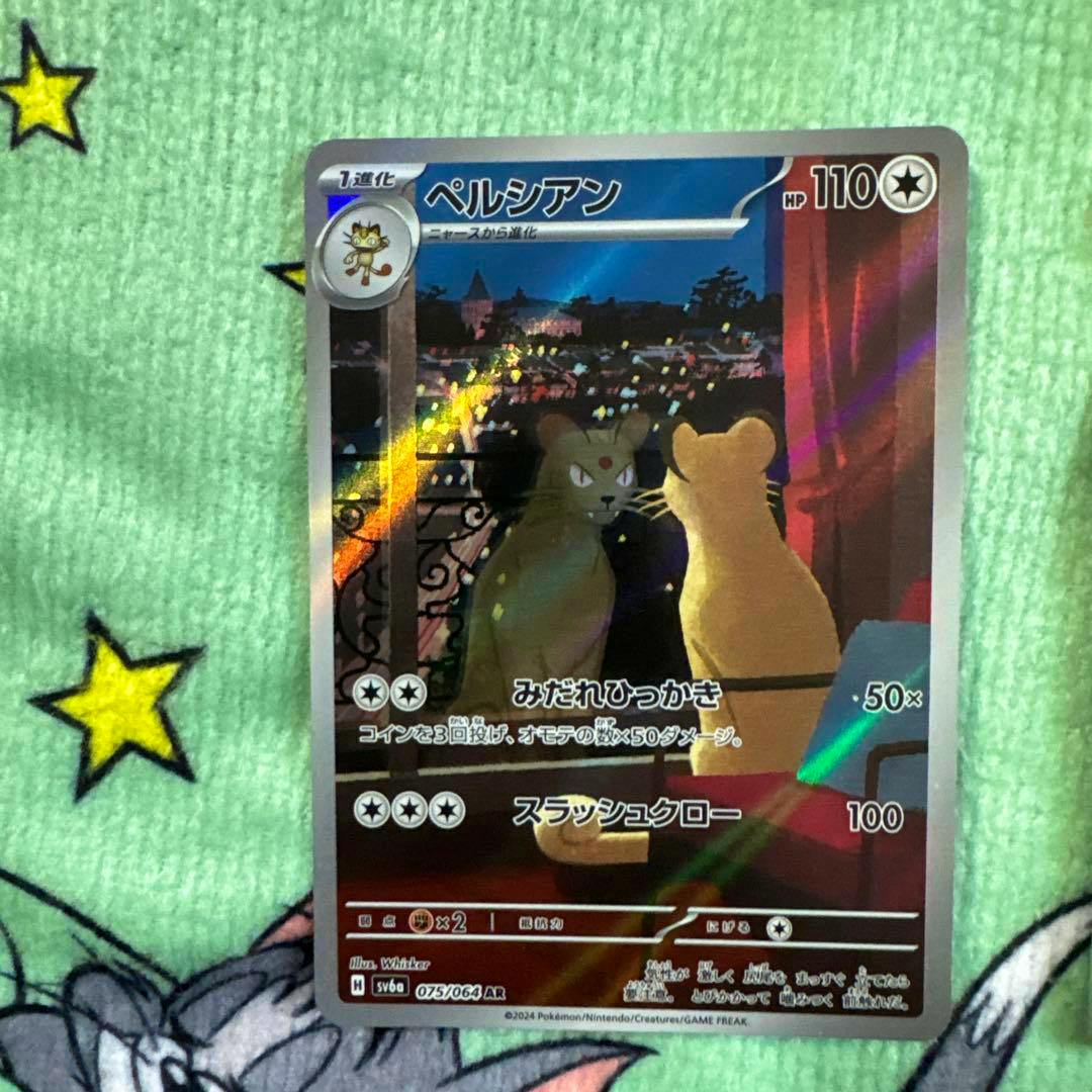 Close-up photo of a holographic Pokémon trading card (ペルシアン) from the Scarlet & Violet series placed on a green star-patterned cloth.