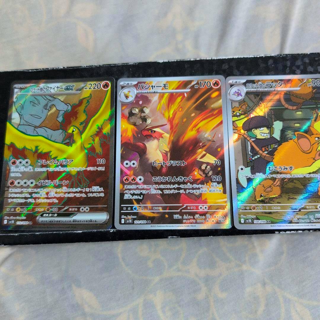 Three holographic Pokémon trading cards in sleeves displayed side-by-side: ロケット団のファイヤー (left), バシャーモ (center), and ロケット団のラッタ (right).