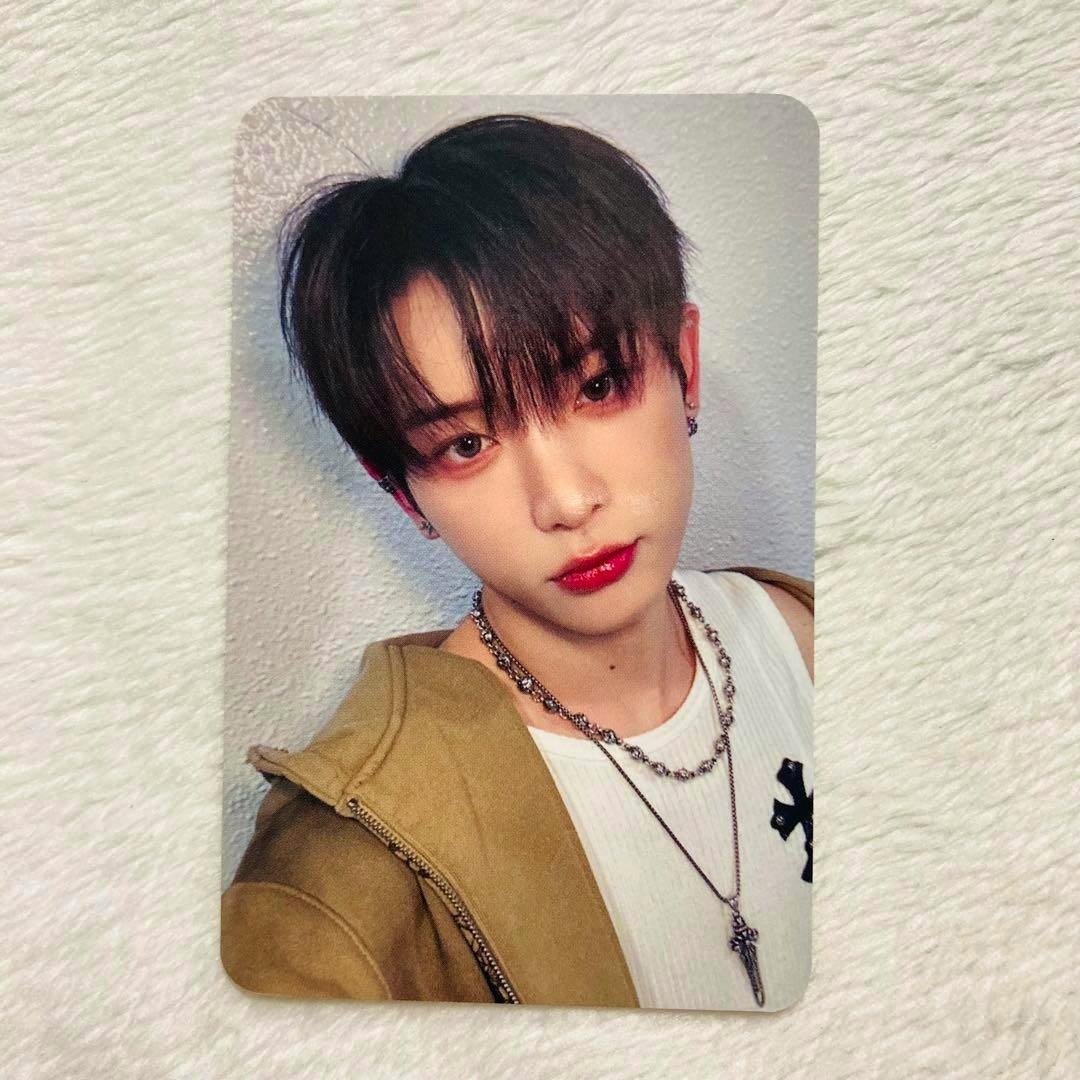 Photocard showing a head-and-shoulders photo of a person wearing layered necklaces and a jacket on a textured background.