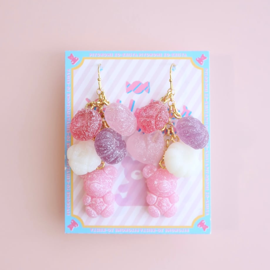A pair of pink teddy bear earrings with multiple translucent candy-like charms displayed on a decorative card.