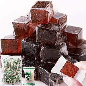 Stacked individually wrapped dark brown konbu black-sugar jelly candy cubes with an inset showing the retail bag and a hand holding one piece.