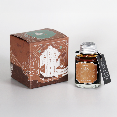 A fountain pen ink bottle labeled "Nostalgic Honey" displayed next to its illustrated brown box on a white background.