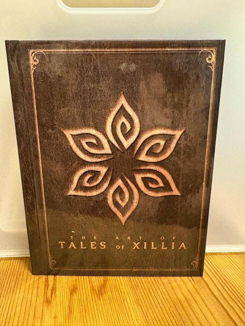 Front cover of THE ART OF TALES OF XILLIA illustration book showing a stylized flower emblem and the title.