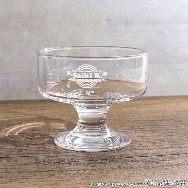 Clear glass dessert cup with a printed "Saiki K." logo shown on a wooden surface.