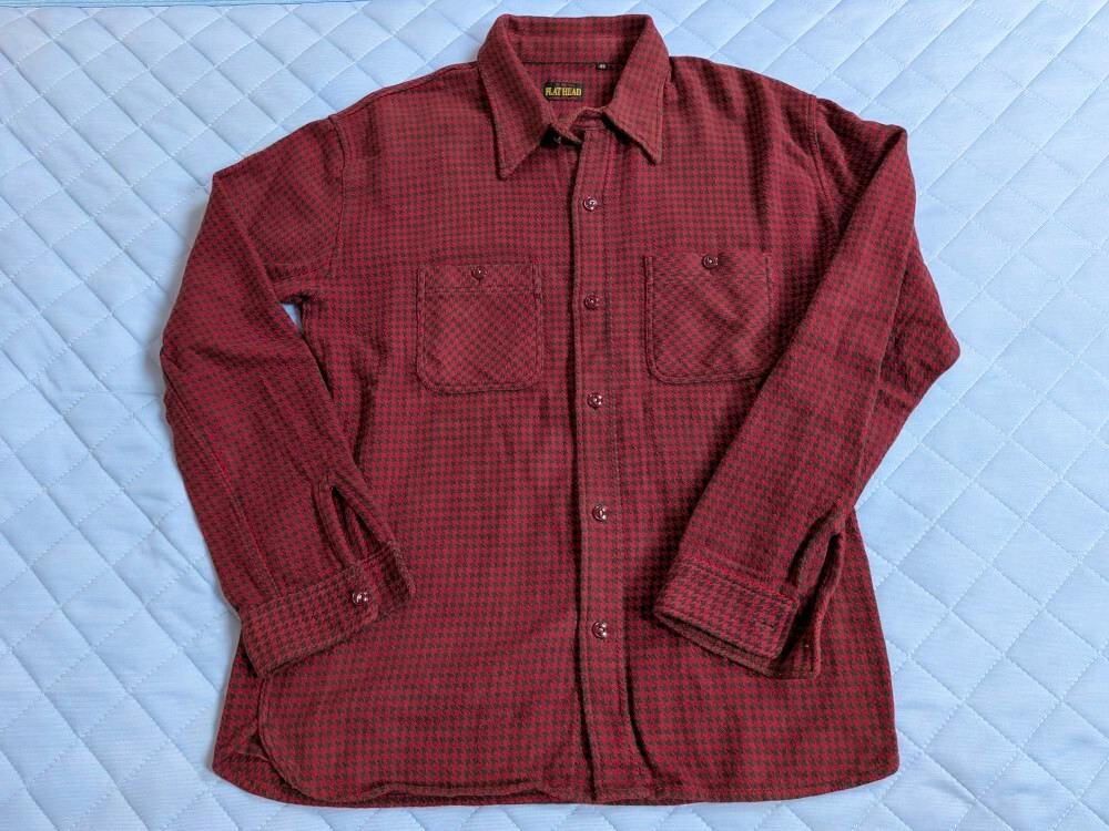 Front view of a red houndstooth long-sleeve shirt laid flat showing button closure and two chest pockets.