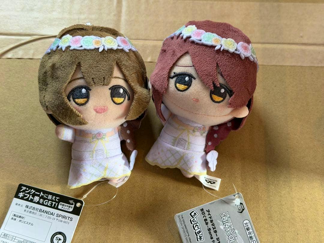 Two chibi plush dolls of シャニマス vol.4 characters 桑山千雪 and 大崎甜花 displayed with their tags on a cardboard surface.