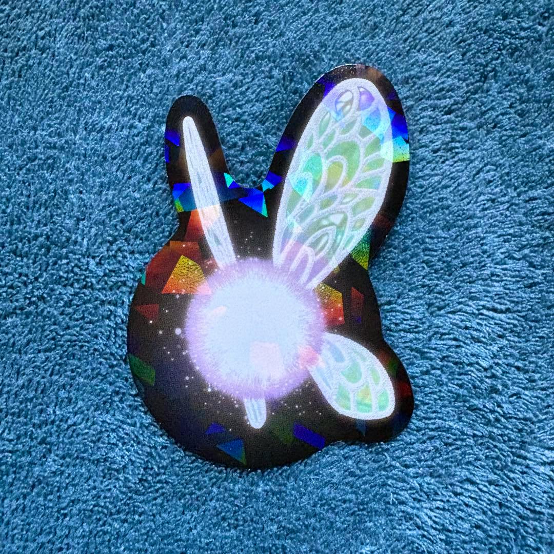 A paper sticker of Navi from The Legend of Zelda with holographic wings placed on blue fabric.