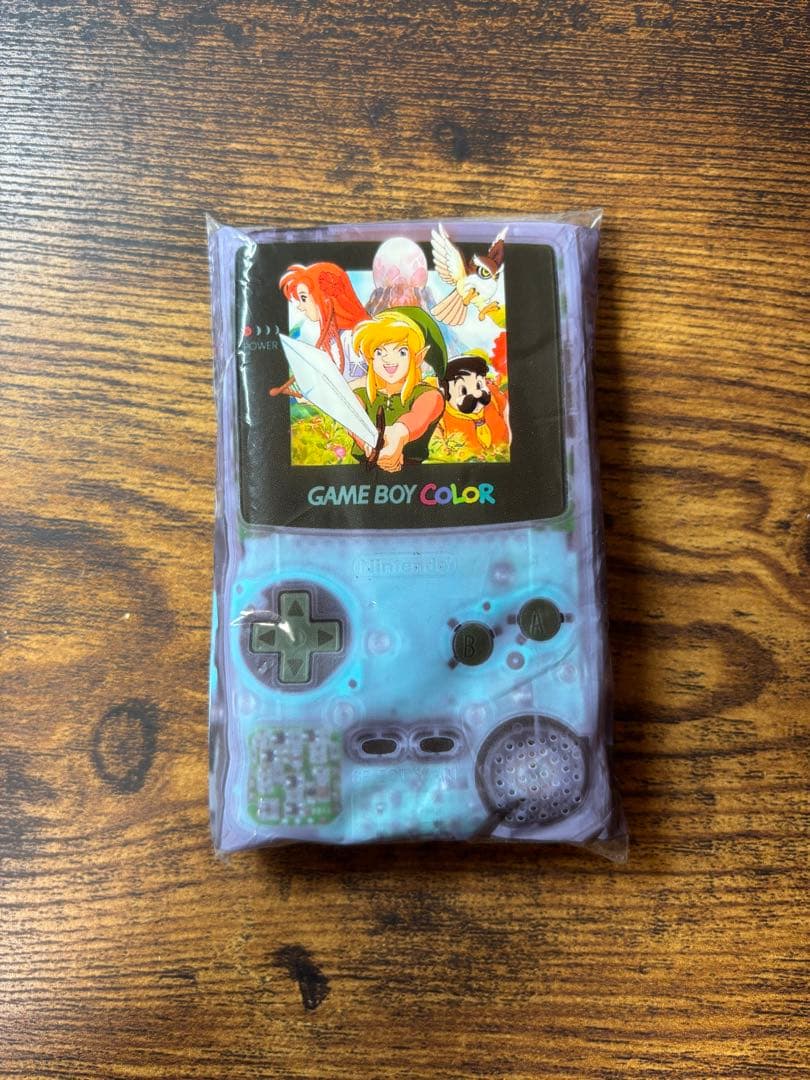 Front view of a sealed pocket tissue pack shaped like a translucent Game Boy Color with artwork from ゼルダの伝説 夢をみる島DX on the screen.