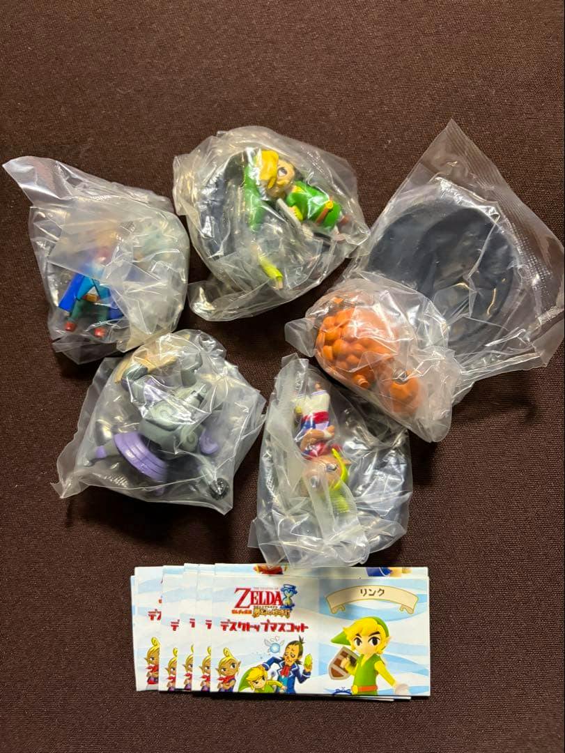 Five unopened The Legend of Zelda: Phantom Hourglass desktop mascot plastic figures, each in a clear bag, shown with paper inserts on a dark background.