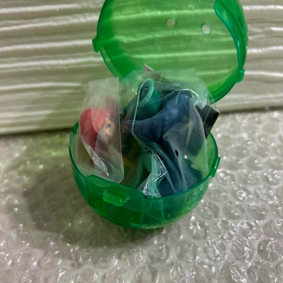Ariel diorama figure pieces visible in sealed plastic bags inside a green capsule case.