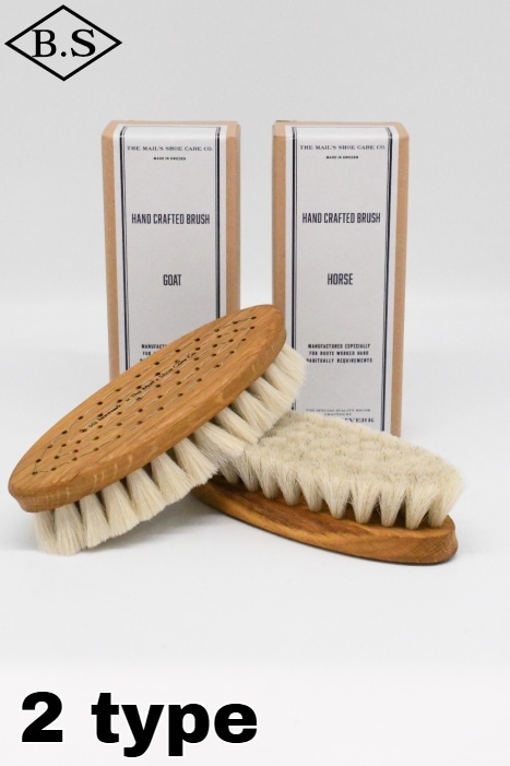 Two hand-crafted shoe cleaning brushes with wooden bases and light bristles displayed in front of two product boxes.