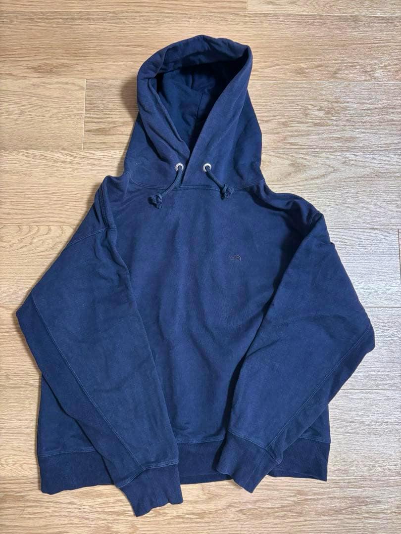 Front view of a navy THE NORTH FACE PURPLE LABEL cotton hoodie laid flat on a wooden floor.