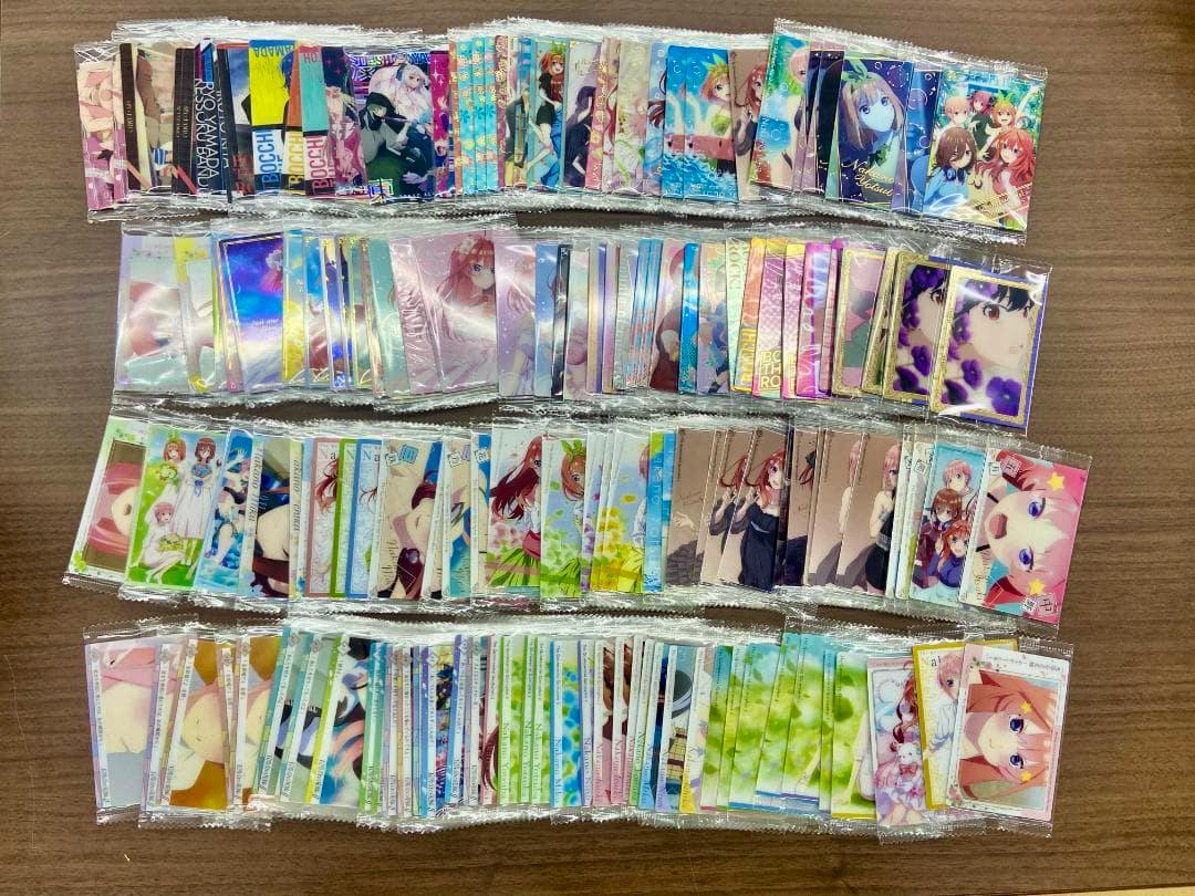Multiple sealed anime photocards and clear cards from the listed series arranged in rows on a wooden table.