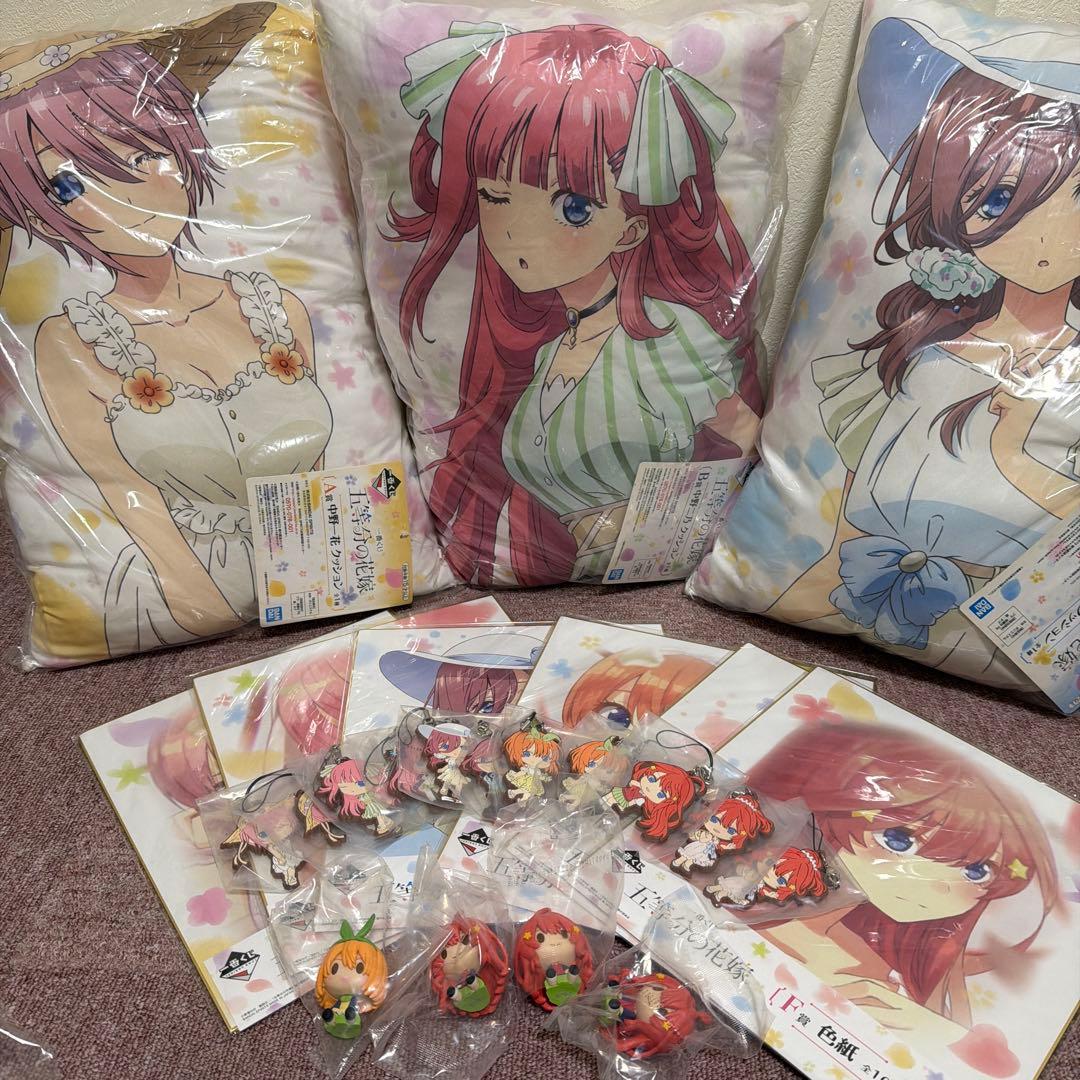 Three cushions with anime character prints and multiple packaged character keychains and cards from the 五等分の花嫁 character goods set arranged on a surface.
