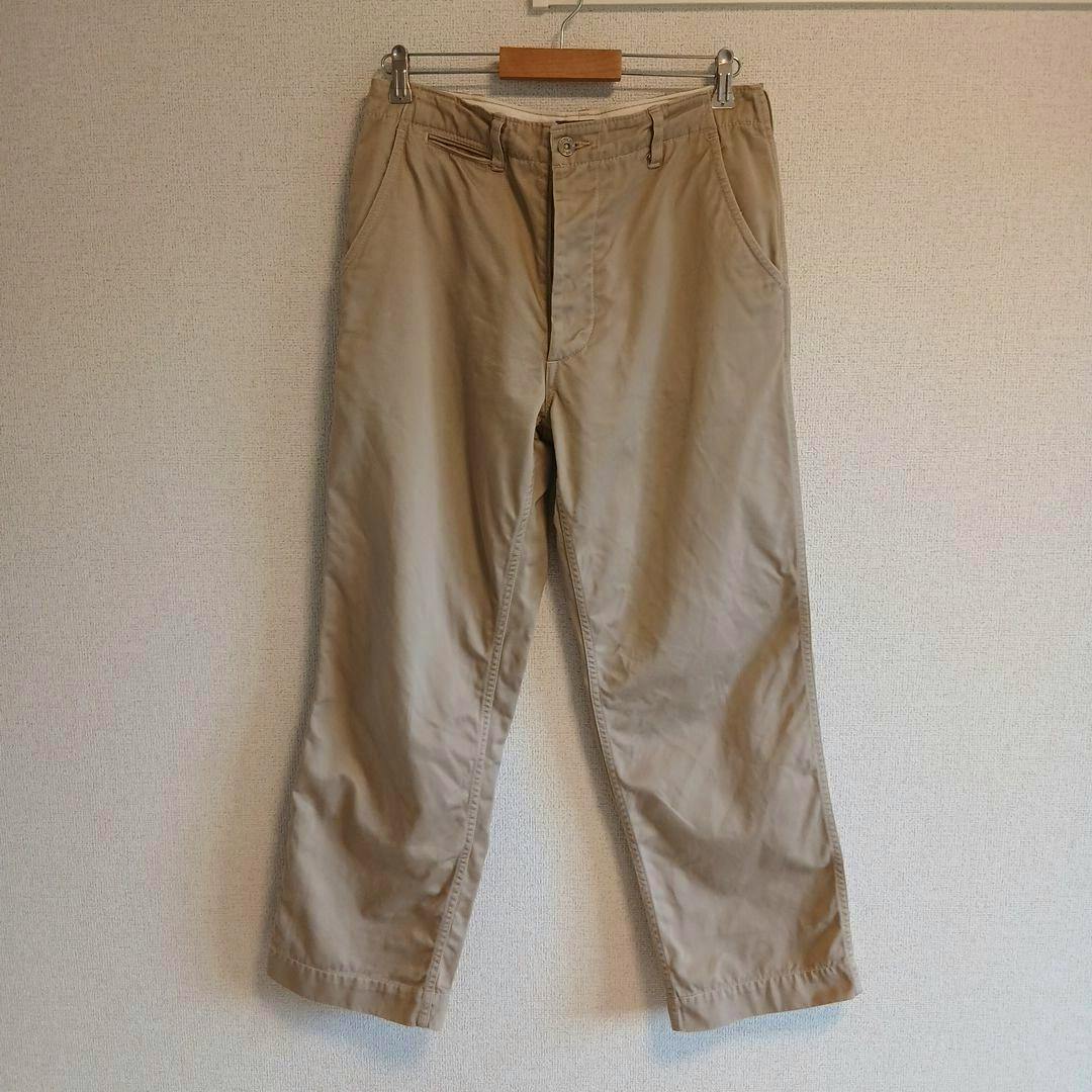 Front view of khaki men's cotton trousers (W32 L34) hanging on a wooden hanger against a beige wall.