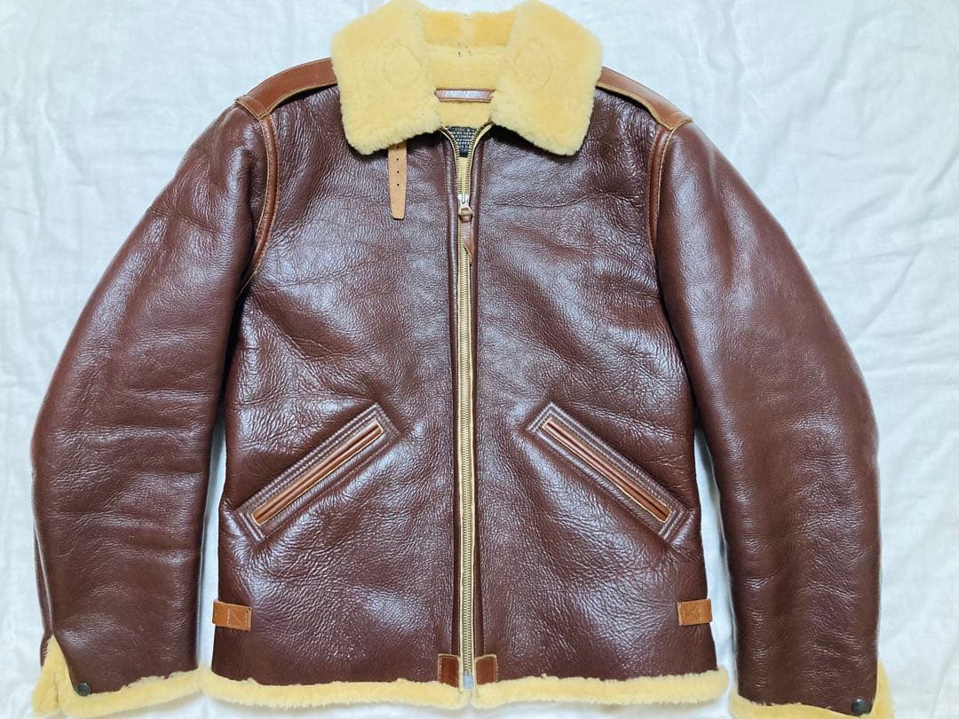 Front view of a brown cow leather B-6 style jacket with yellow shearling collar and hem laid flat.