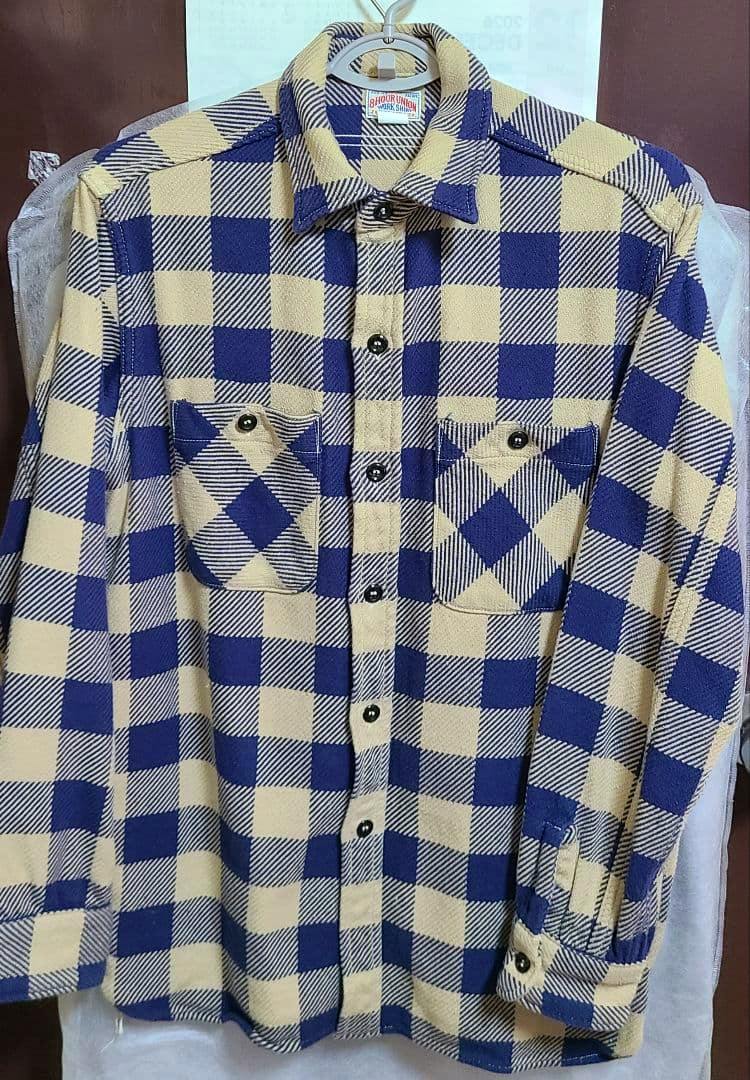 Front view of a men's blue and beige checked flannel shirt hanging on a hanger.