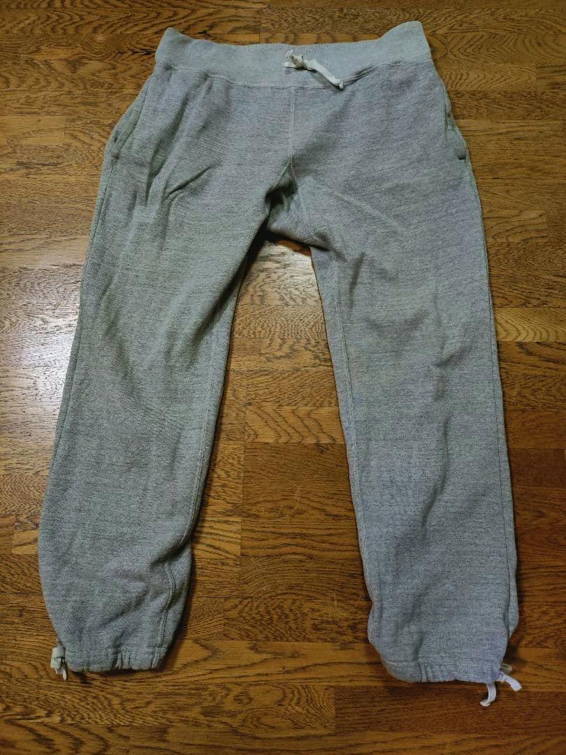 Gray men's sweatpants laid flat on a wooden floor showing the front view.