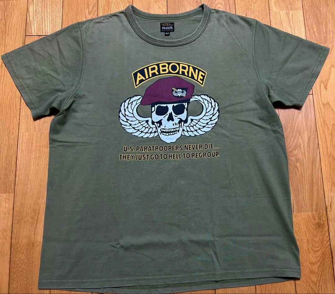 Olive green men's cotton T-shirt laid flat showing an "AIRBORNE" skull-and-wings graphic and chest text.