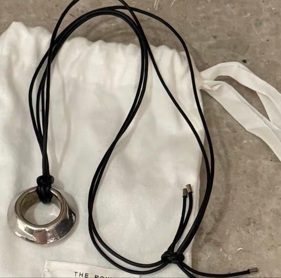 Silver circular pendant necklace on a black cord laid on a white cloth pouch.