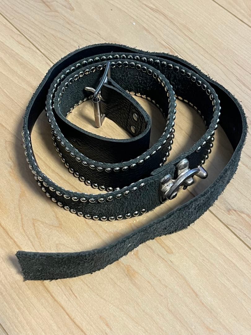Coiled black studded cow leather belt with metal buckle and round studs on a wood floor.
