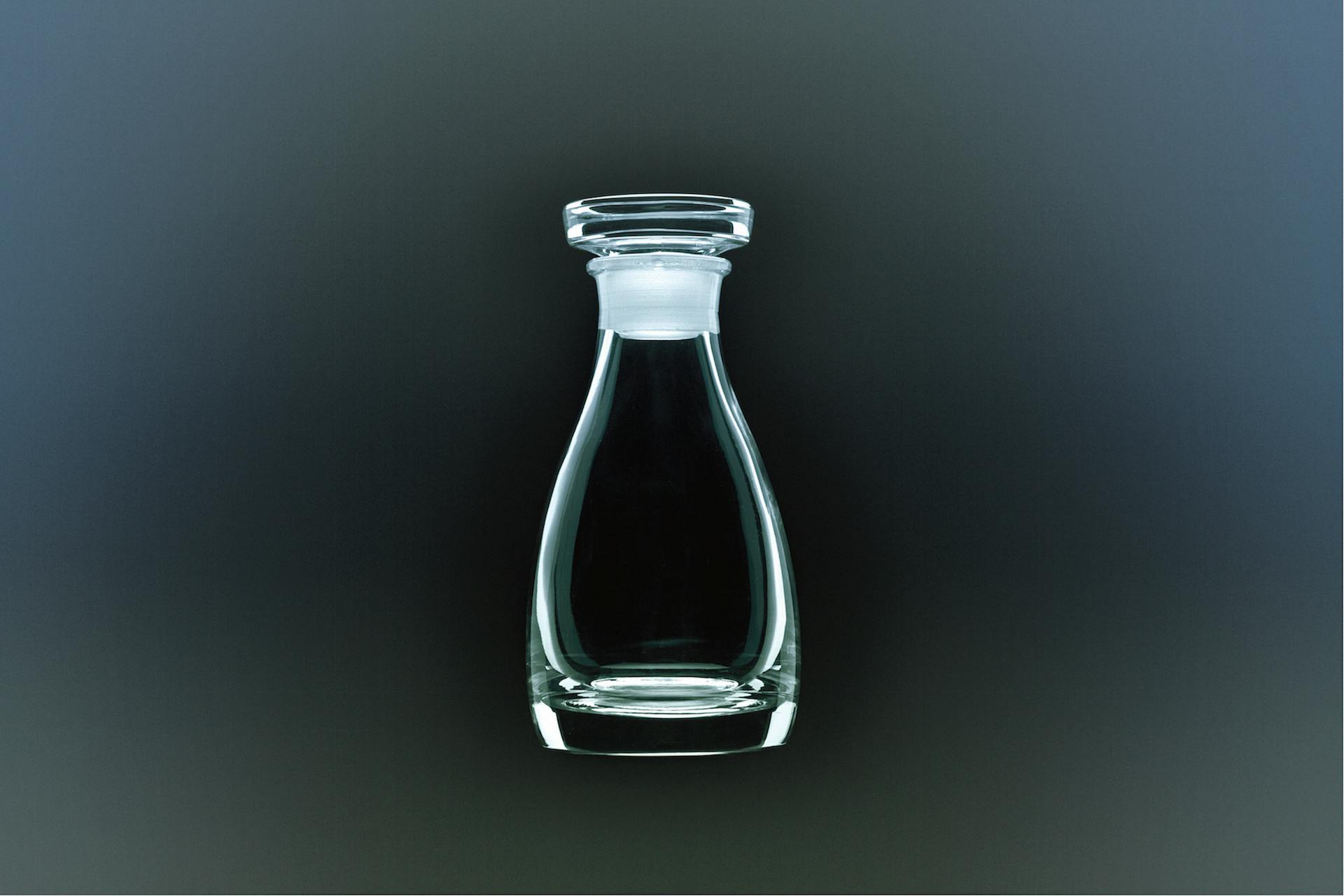 Top portion of a clear glass soy sauce bottle (THE 醤油差し) shown against a dark background.