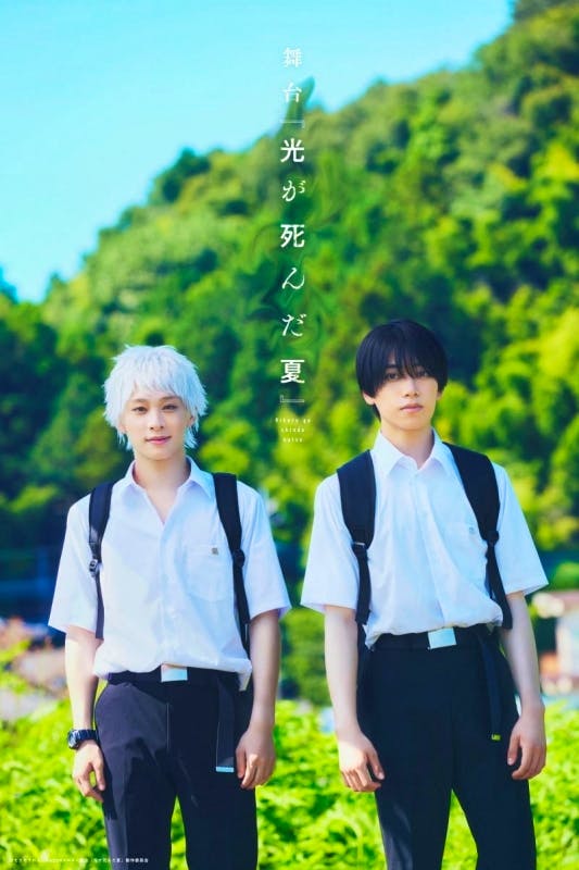 Blu-ray cover-style photo of two young men in white school shirts and backpacks standing outdoors with trees in the background.