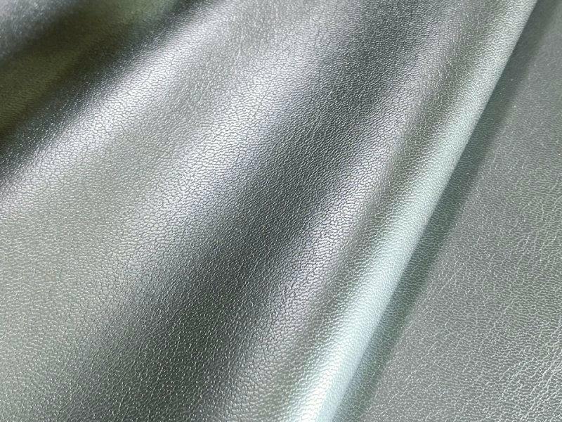 Close-up of silver shiny thin synthetic leather (PU) fabric showing grain texture and drape.
