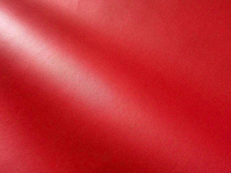 Red synthetic leather (polyester) fabric with a soft fold and fine grain texture visible.