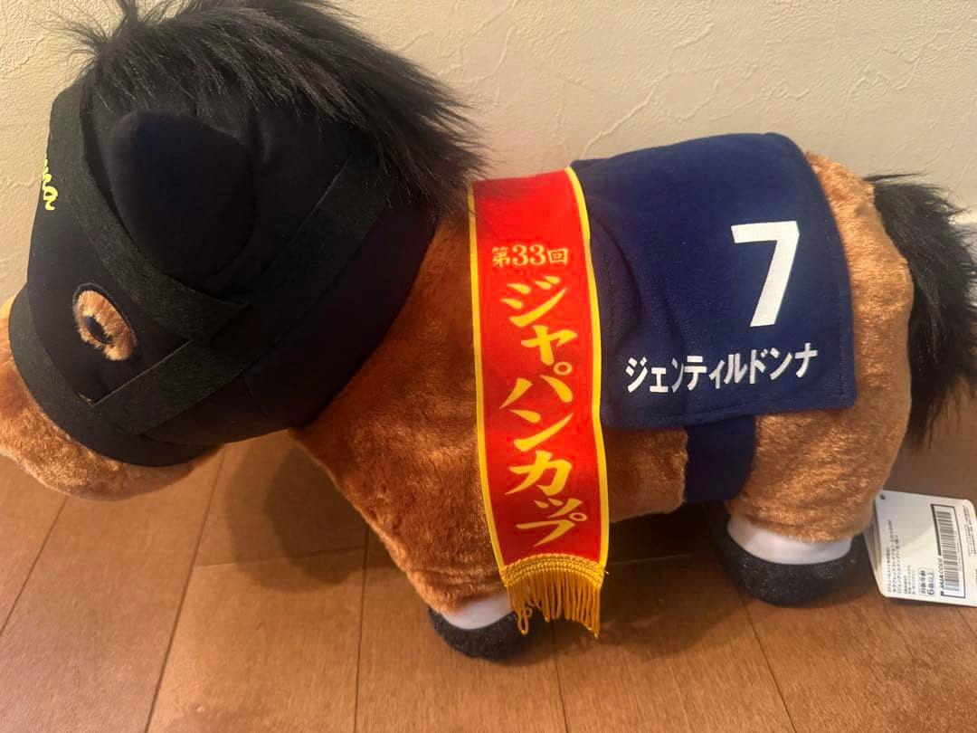 Brown plush horse toy labeled ジェンティルドンナ wearing a blue saddlecloth with the number 7 and a red sash.