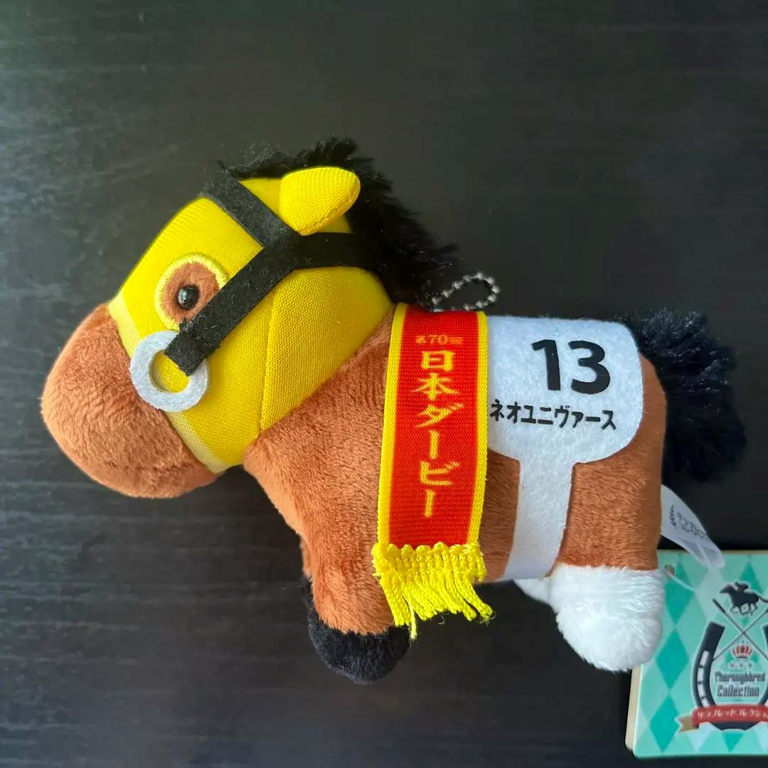 Side view of the plush ball-chain keychain horse (Neo Universe) wearing a yellow bridle and a red sash showing the number 13.