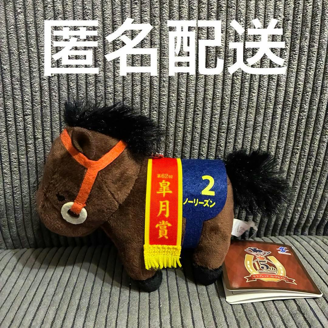 A brown plush toy horse wearing a blue saddle cloth labeled "2" and a red ribbon sash, photographed on a gray striped fabric.